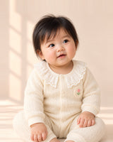 Baby sitting in the Lily cream knit romper with a lace ruffle collar – Cream
