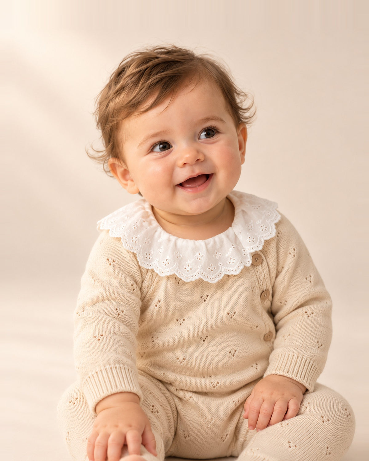 Baby sitting in the Pearl oatmeal pointelle jumpsuit with a white eyelet collar – Oatmeal