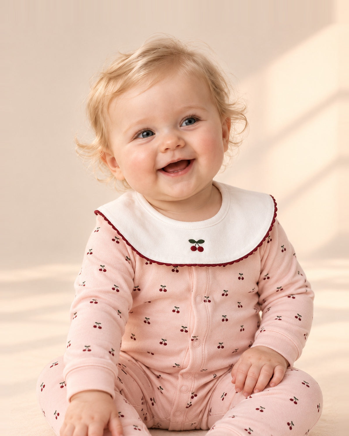 Baby sitting and laughing in the Ruby pink cherry romper with a white collar – Pink Cherry