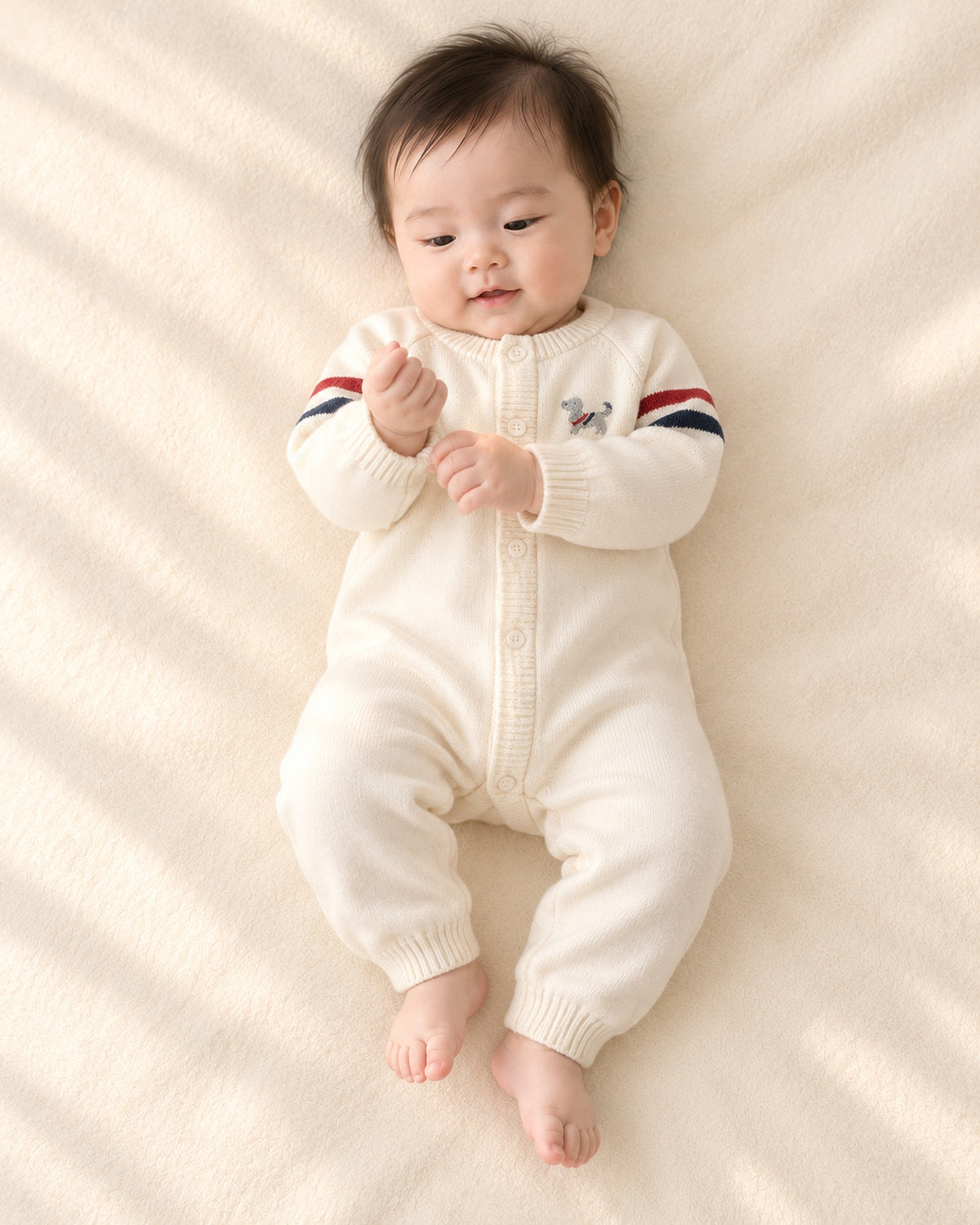 Baby lying in the Benji cream puppy knit jumpsuit with striped sleeves – Cream
