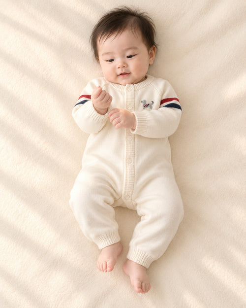 Baby lying in the Benji cream puppy knit jumpsuit with striped sleeves – Cream