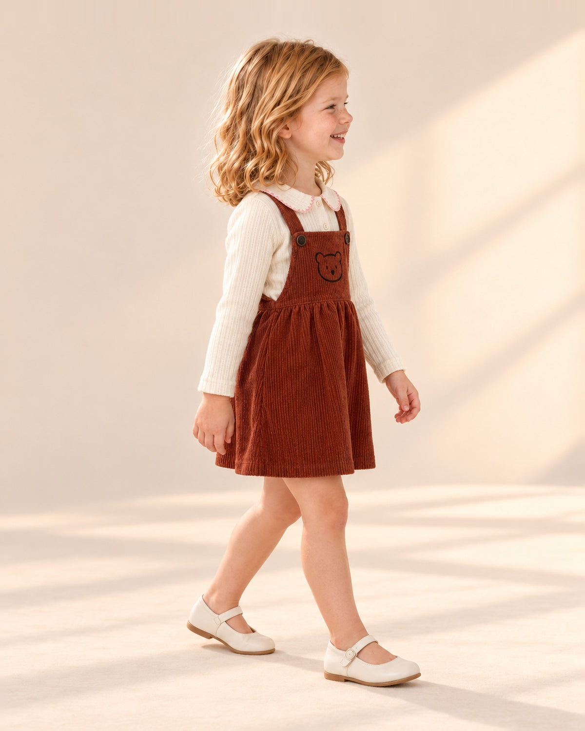 Side view showing the fitted rib sleeve under the rust corduroy pinafore – Cream
