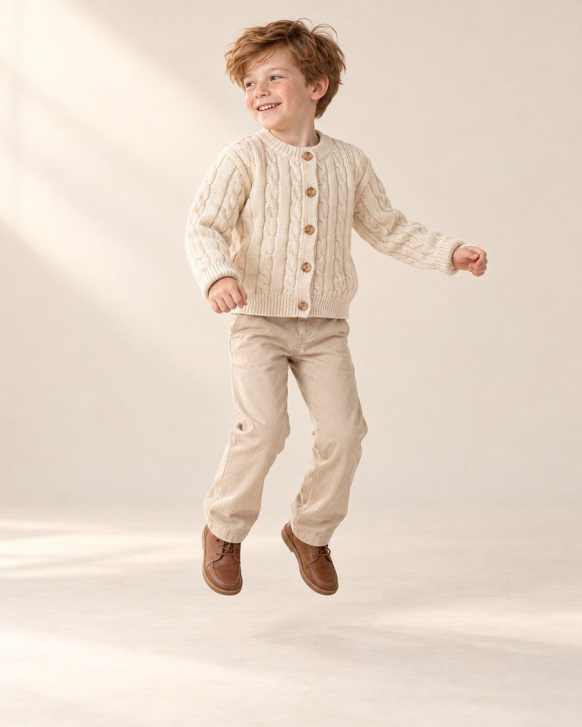 Boy jumping in the cream cable knit cardigan – Cream