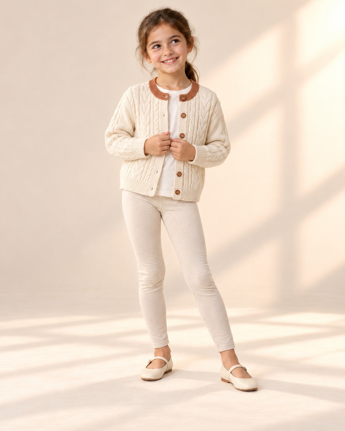 Girl smiling and holding the front of the cream cable cardigan – Cream