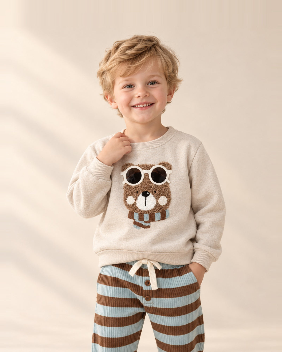 Boy smiling in the Monty bear sweatshirt with striped pants – Oatmeal