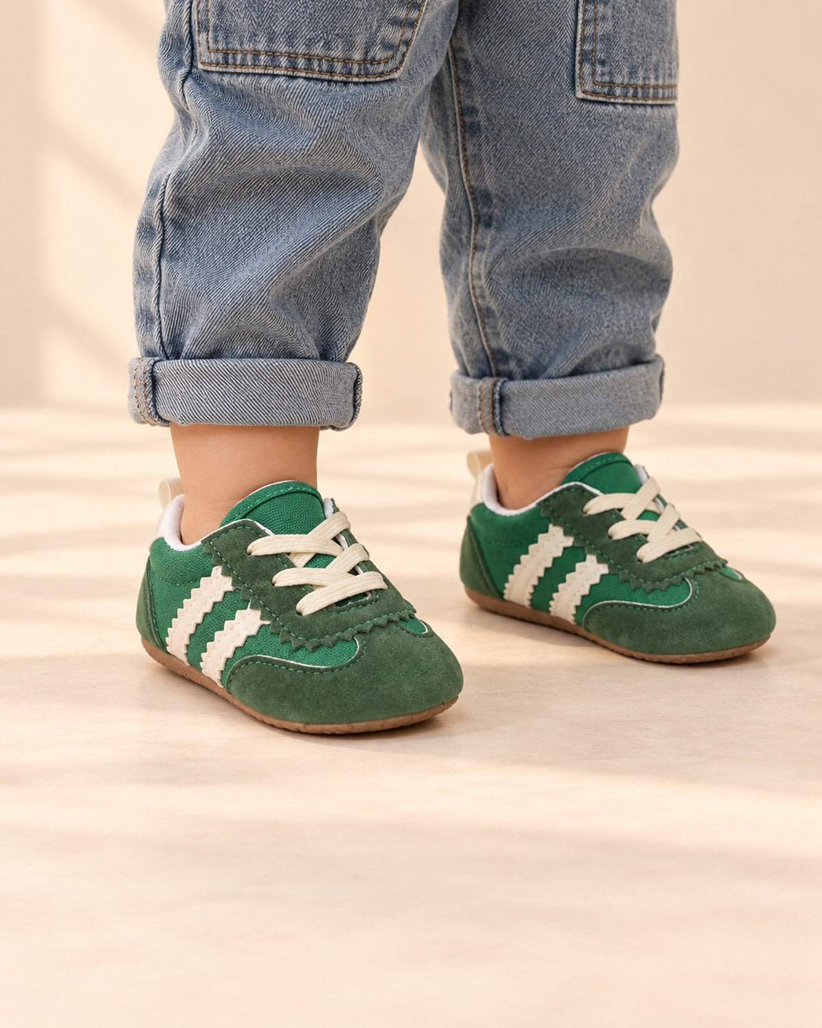 Close-up of green suede-look baby sneakers with cream stripes and laces – Green