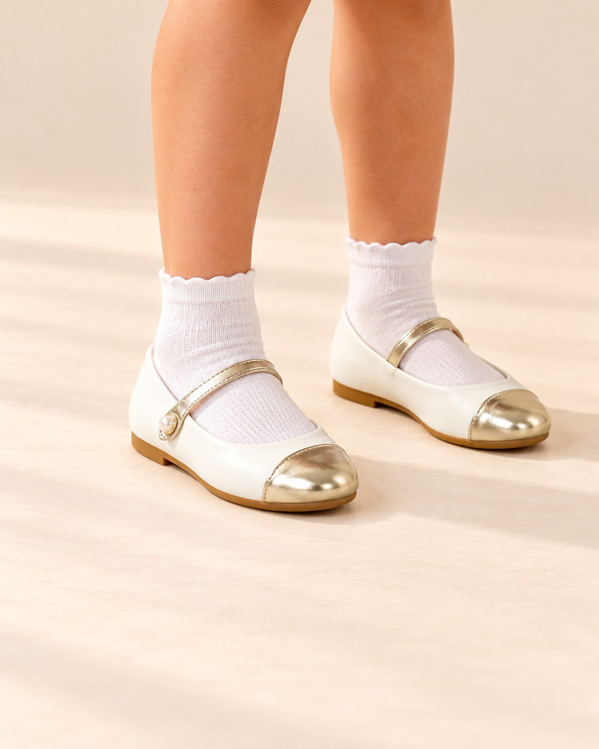 Close-up of white Mary Jane flats with gold toe caps and a pearl strap – White