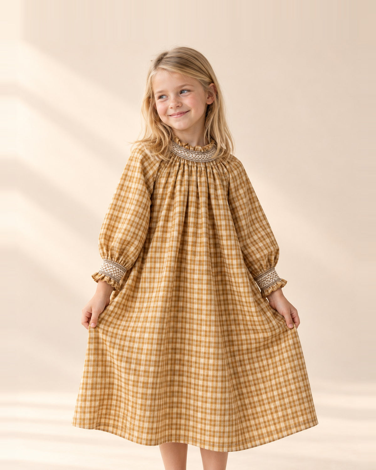 Girl holding out the skirt of the Marigold ochre check smock dress – Ochre Check