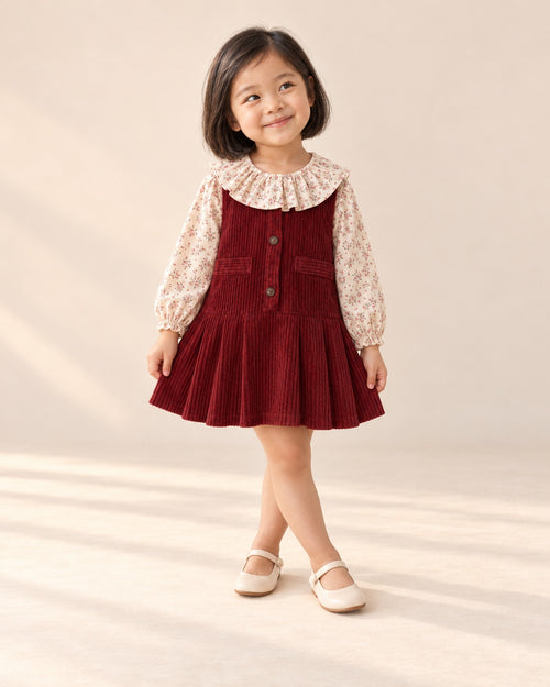Girl standing with crossed feet in the red corduroy pinafore – Deep Red