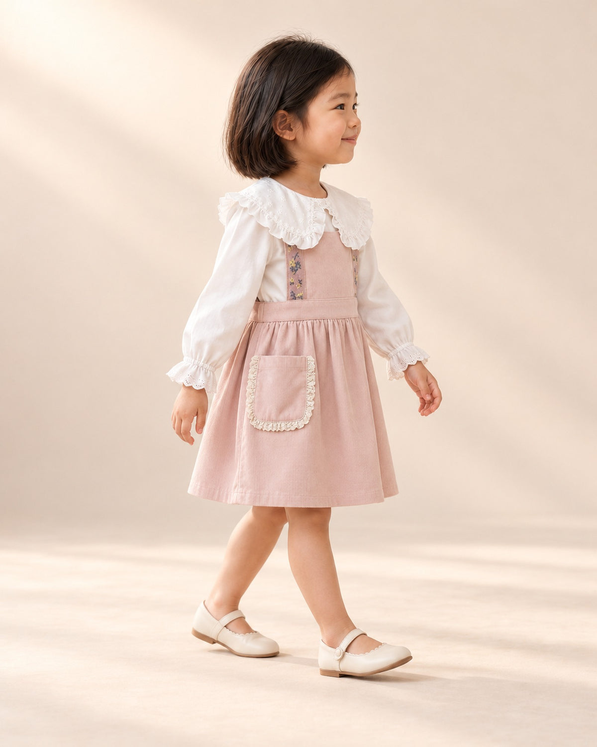 Side view of the lace pocket corduroy pinafore worn with the ruffle collar blouse – Pink