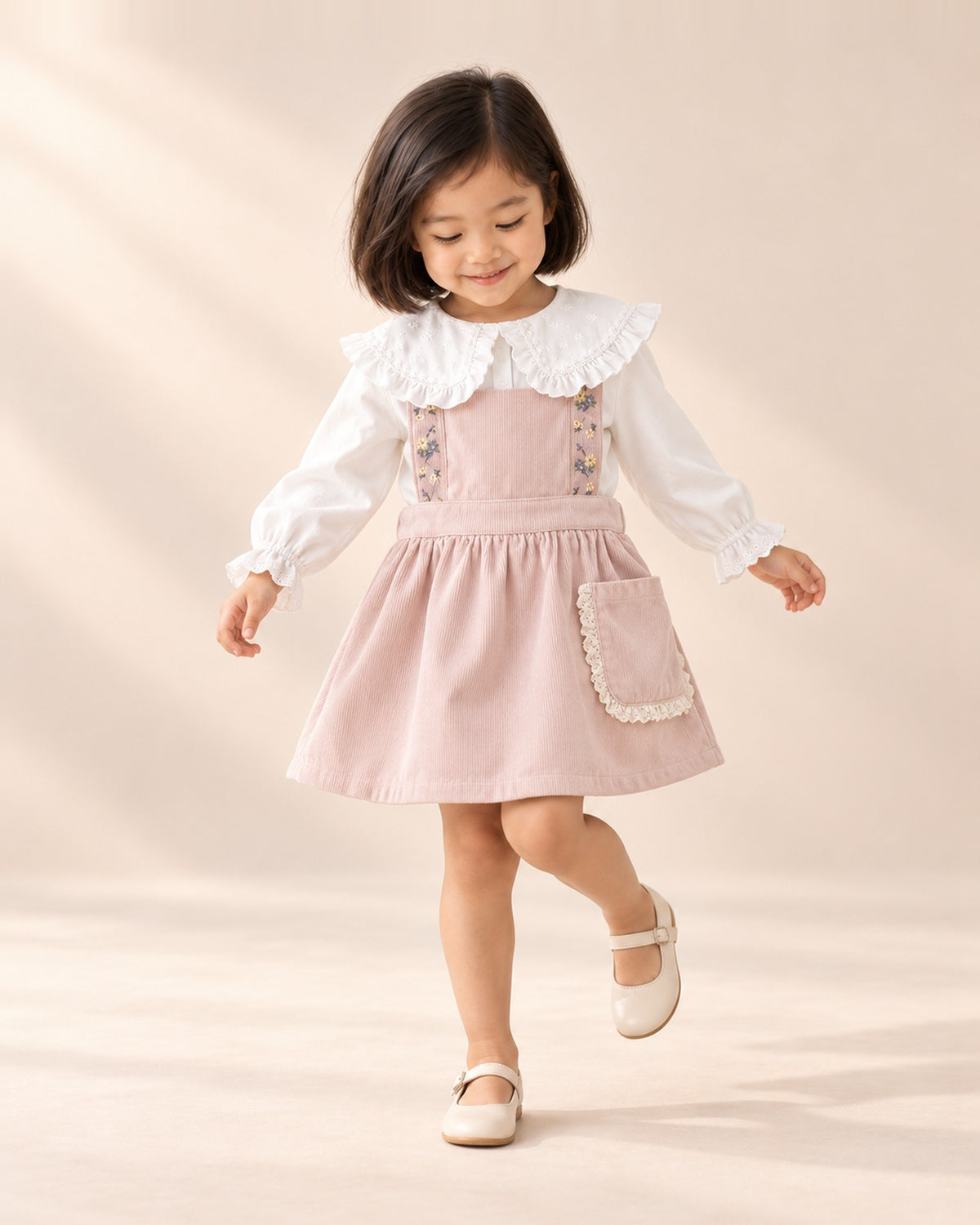 Girl at play in the lace pocket corduroy pinafore, styled with the ruffle collar blouse – Pink