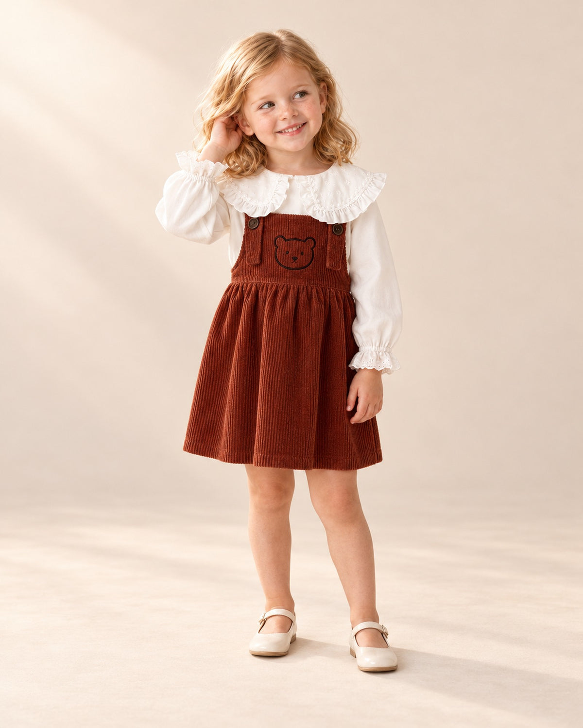 Full-length front view of the rust pinafore with embroidered teddy bear, paired with the ruffle collar blouse – Rust