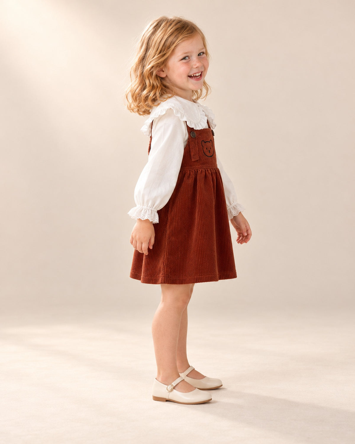Side view of the rust pinafore with embroidered teddy bear worn with the ruffle collar blouse – Rust