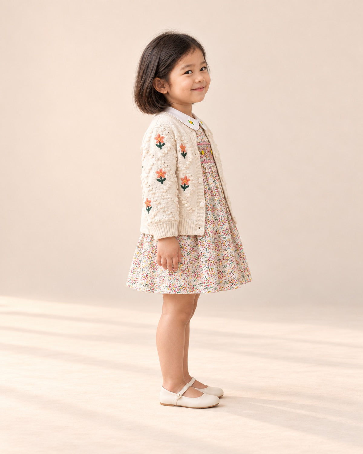 Side view of the embroidered flower knit cardigan worn with the smocked floral dress – Cream