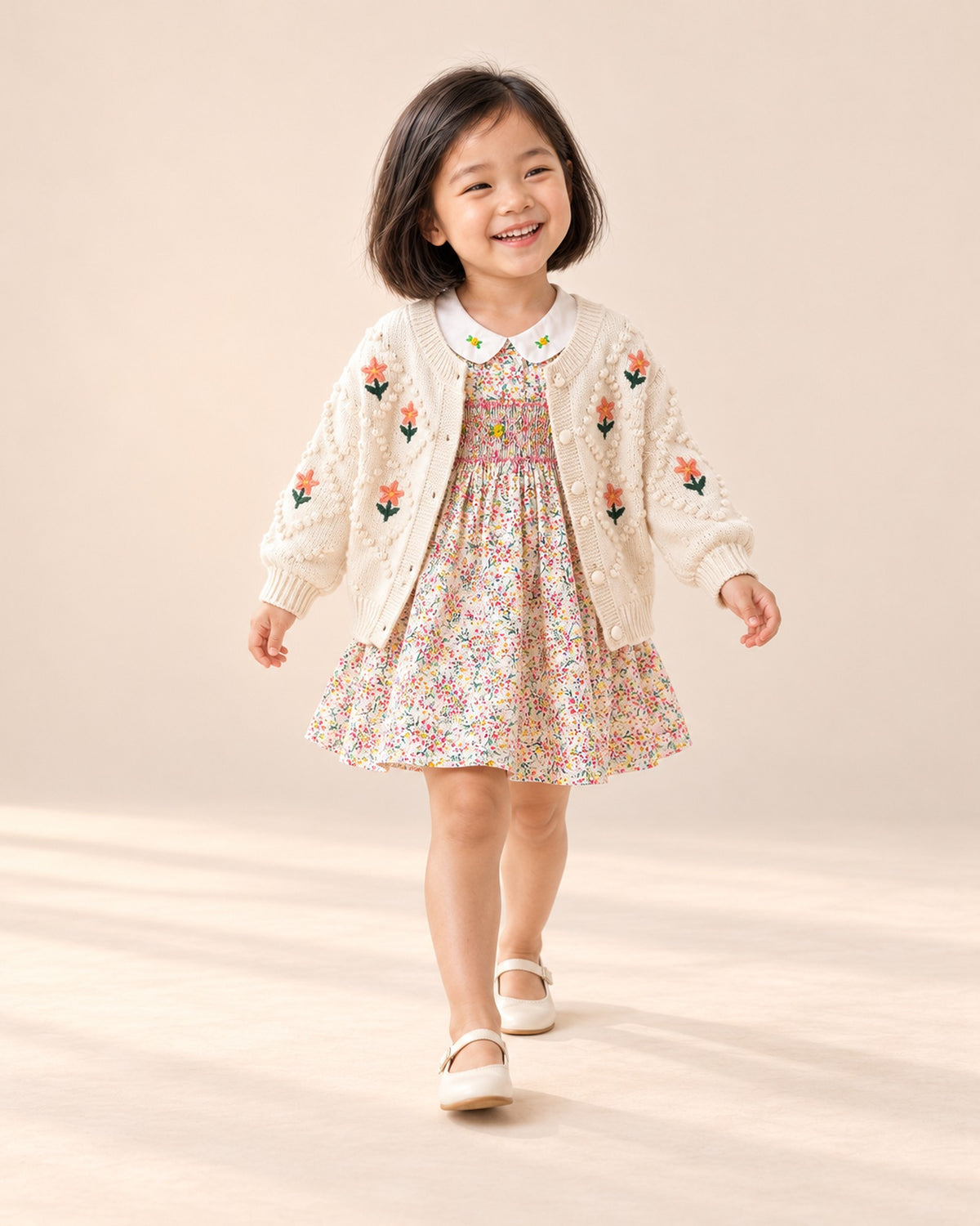 Girl at play in the embroidered flower knit cardigan, styled with the smocked floral dress – Cream