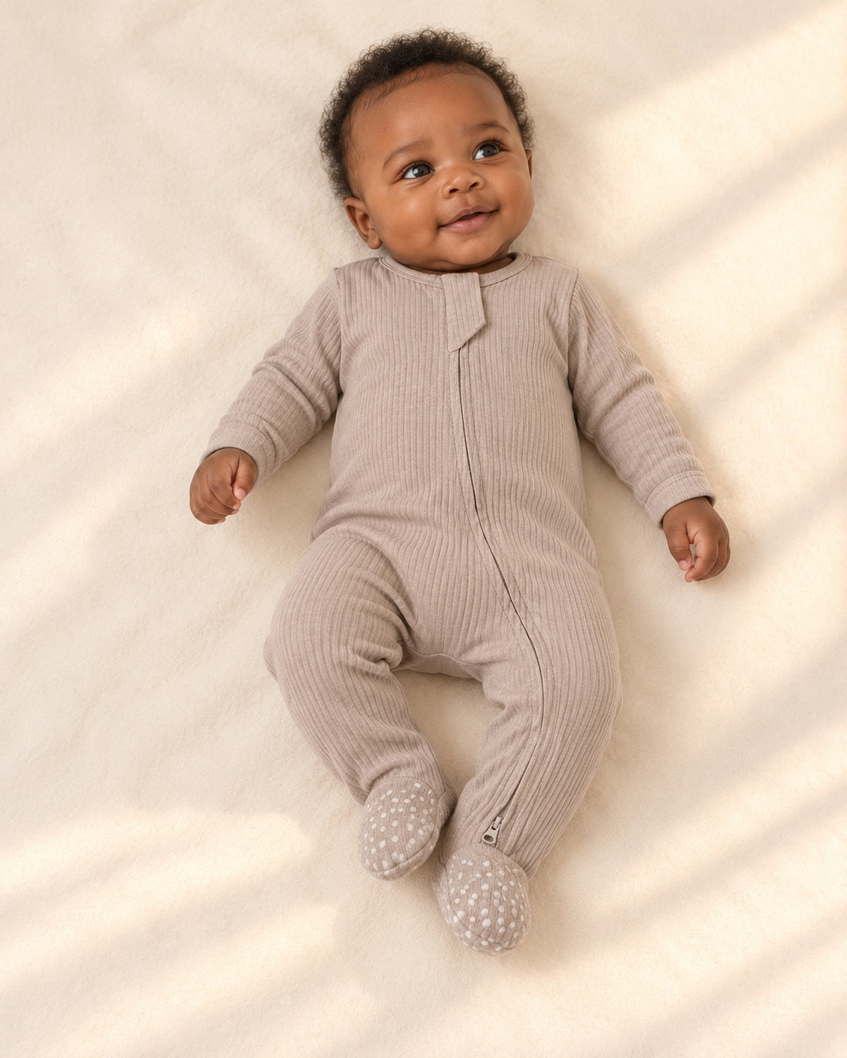 Baby lying in the Cubby taupe ribbed zip footie – Taupe