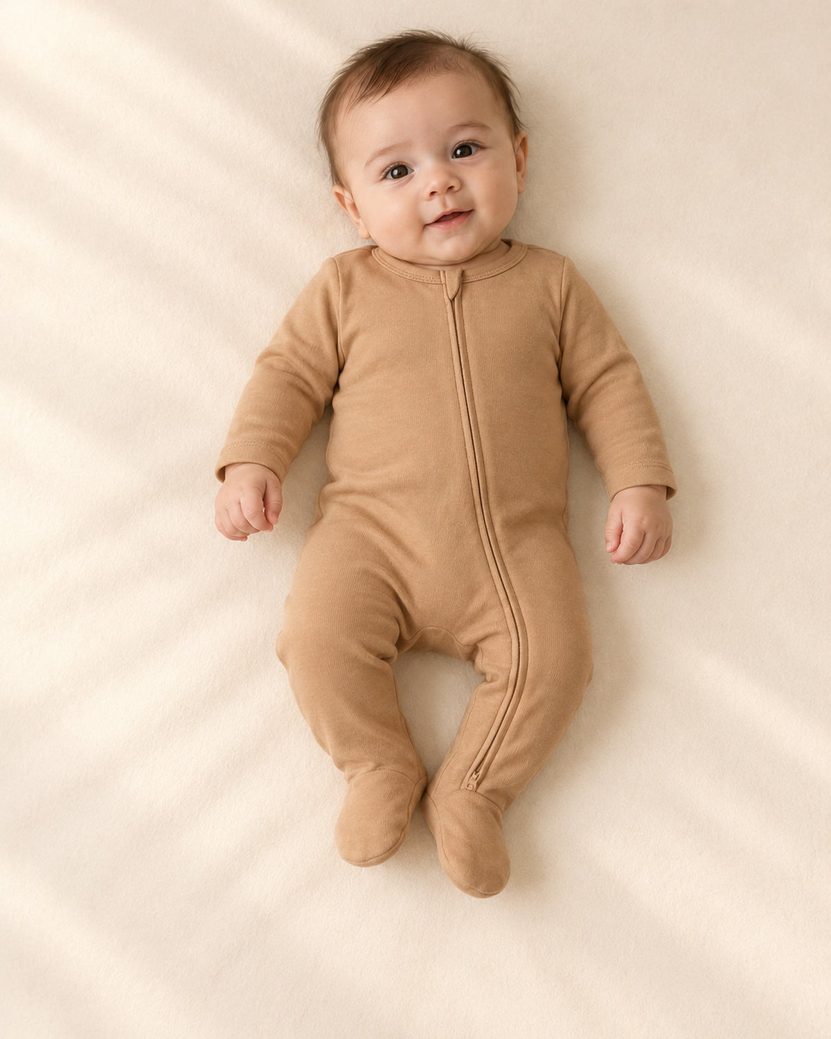 Front view of a baby in the camel zip footie and a cream bear-ear beanie, full length – Camel