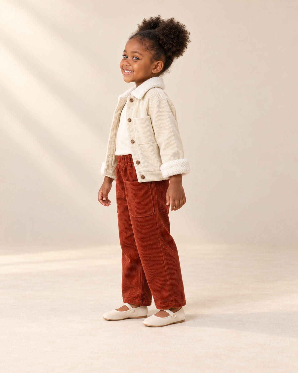 Side view of the rust pants showing the patch pocket and wide leg, with the cream jacket – Rust