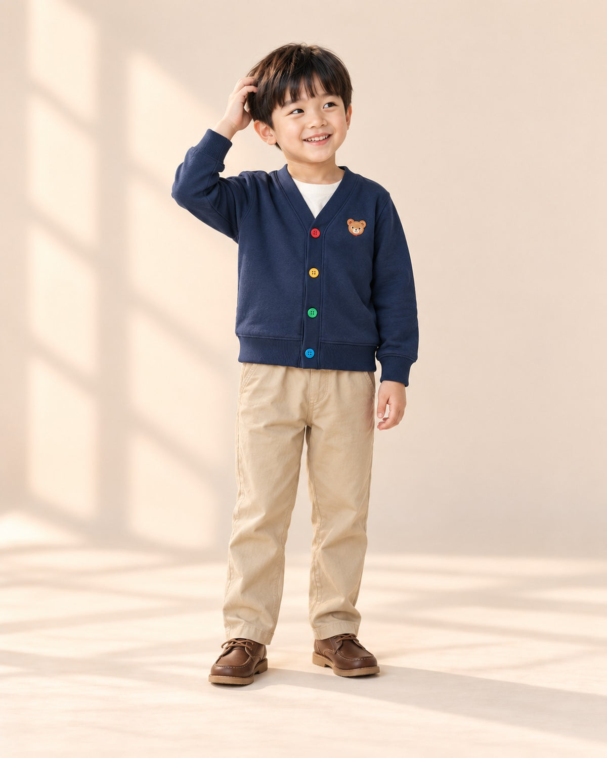 Front view of a boy in khaki chinos and a navy cardigan with rainbow buttons – Khaki