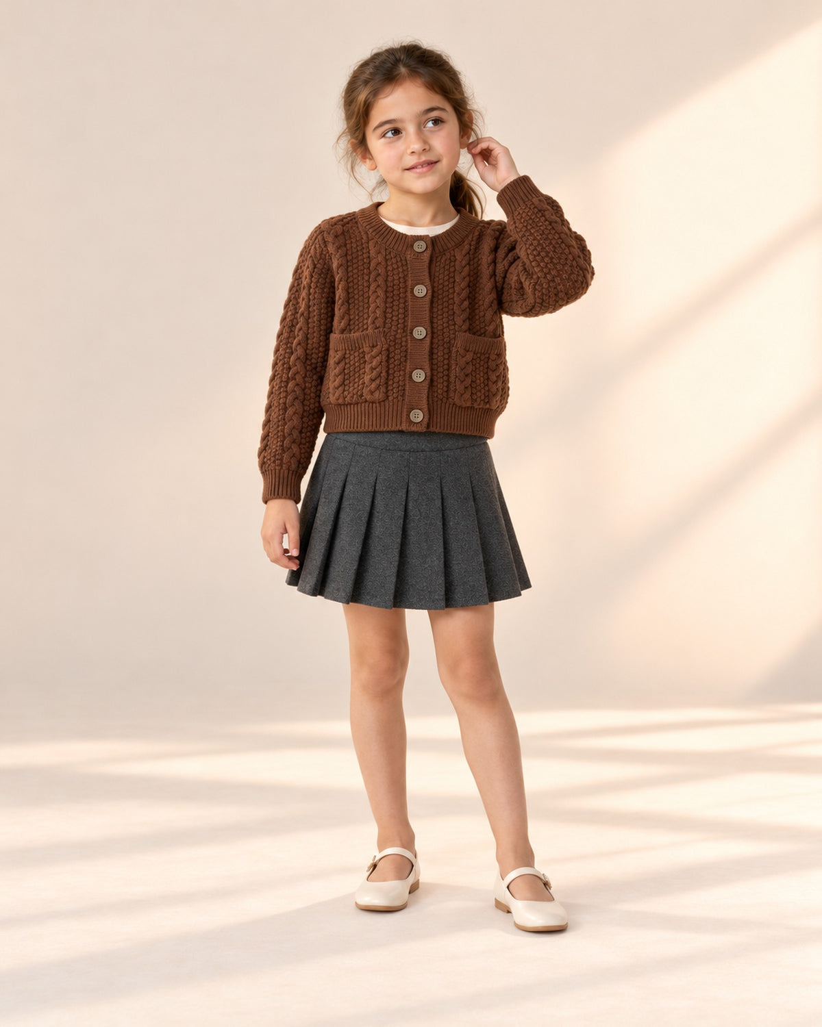 Front view of a girl in the charcoal pleated skirt and a chocolate cable cardigan over a cream top, full length – Charcoal