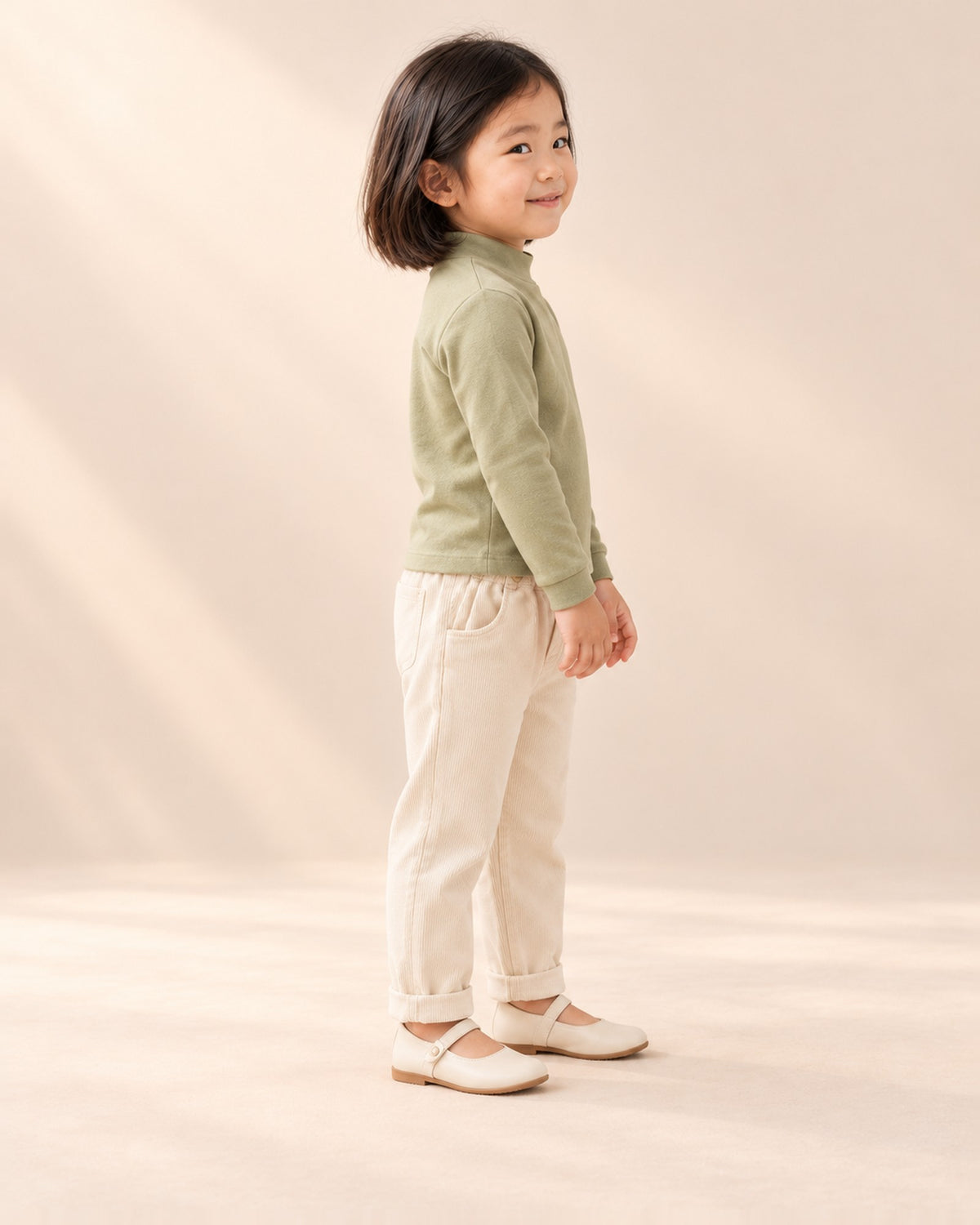 Side view of the sage mock-neck top showing the fitted sleeves and soft mock neck, worn with cream corduroy pants – Sage