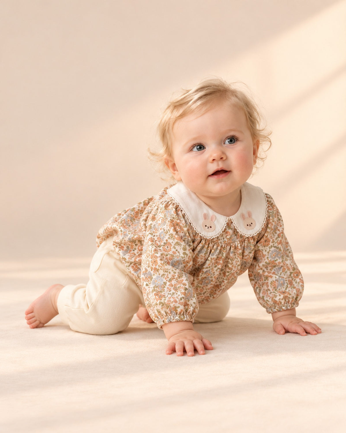 Baby in the cream pants and floral bubble romper, shown relaxed – Cream