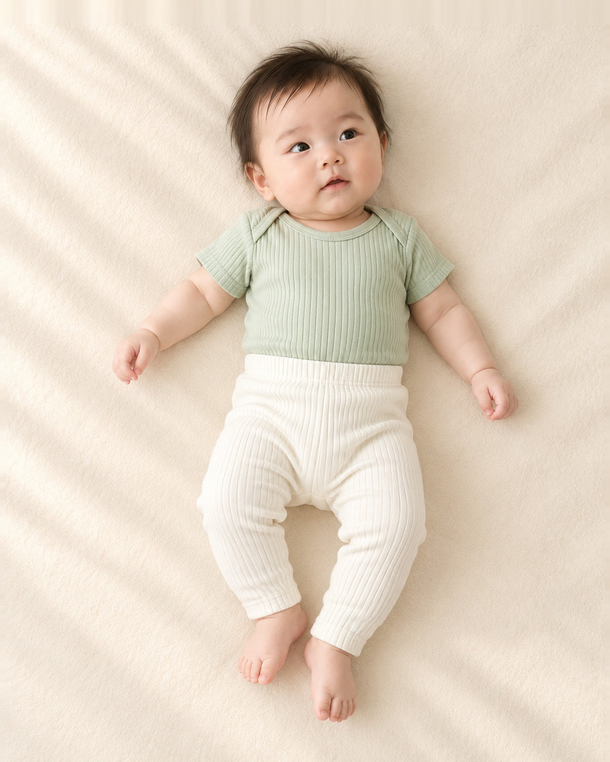 Front view of a baby in the sage ribbed bodysuit and cream ribbed leggings, full length – Sage