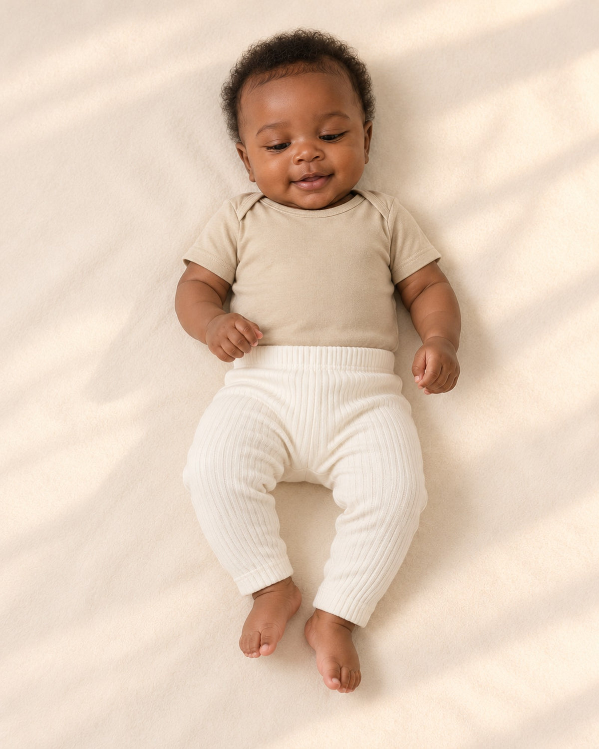 Front view of a baby in the oatmeal bodysuit and cream ribbed leggings, full length – Oatmeal