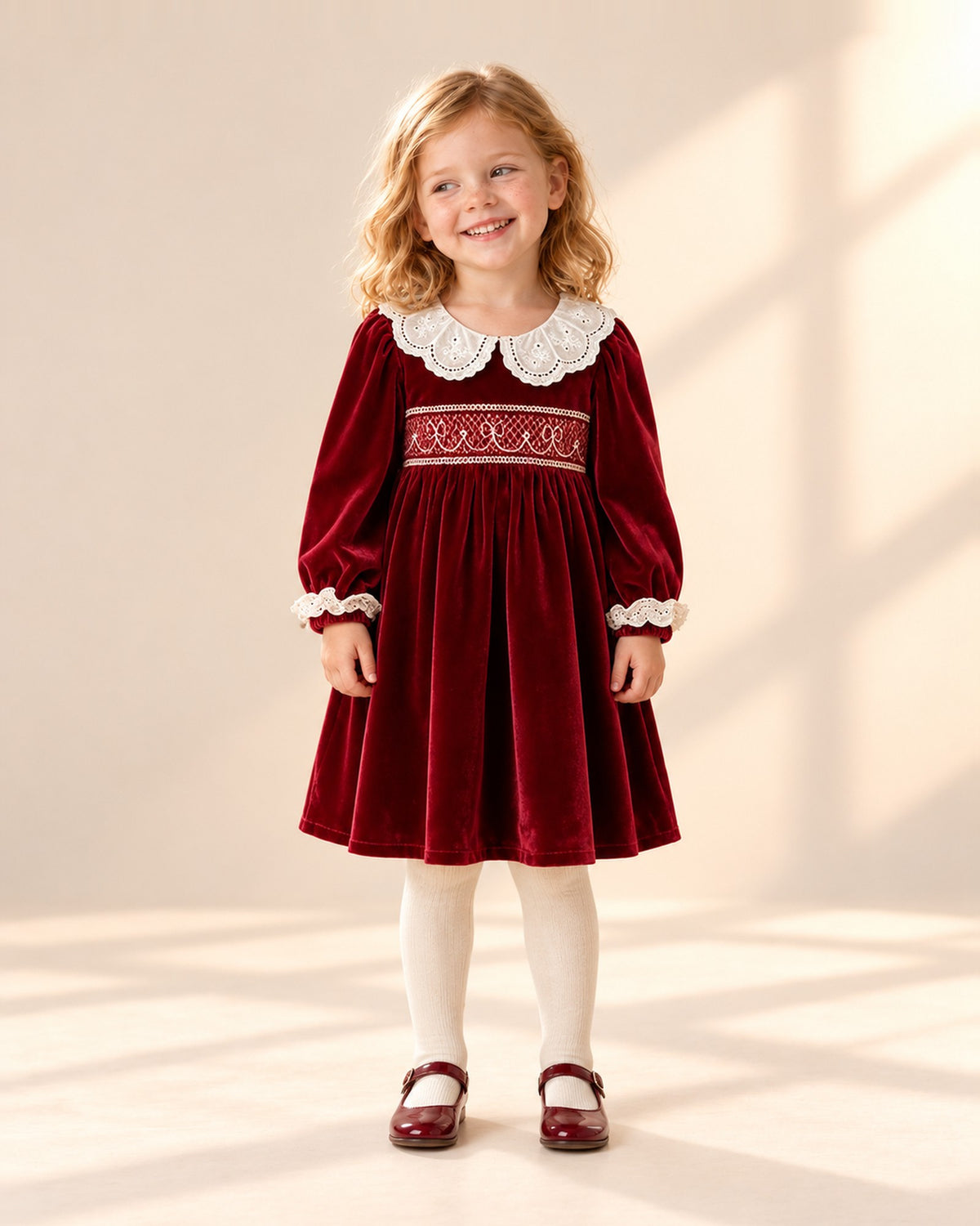Front view of a girl in the velvet smocked dress, cream ribbed tights and burgundy shoes, full length – Red