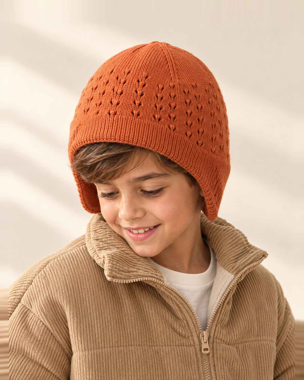Boy wearing the Wilfred rust pointelle earflap hat, head and shoulders – Rust
