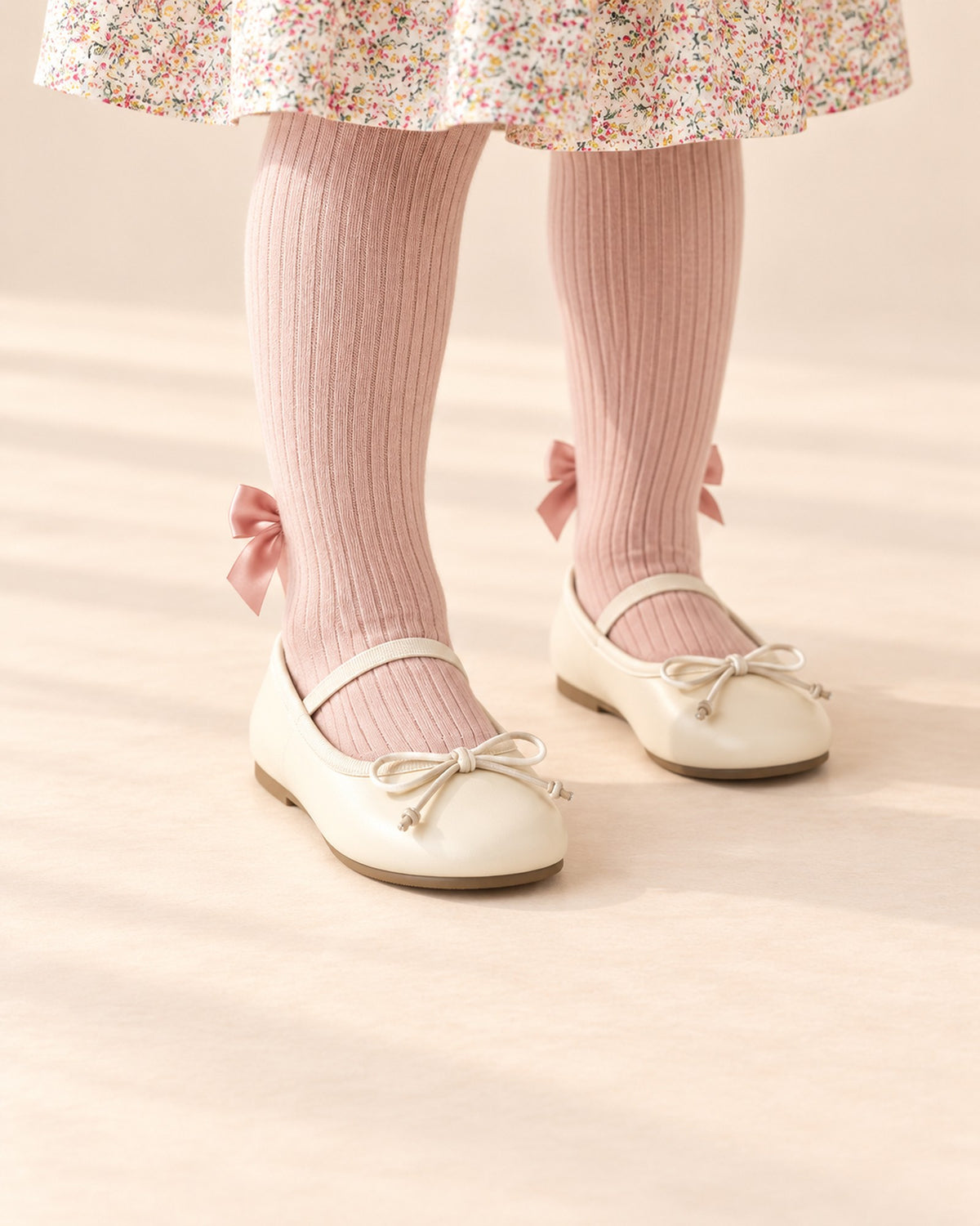 Close-up of a girl's feet in cream ballet flats with a tied bow, worn with blush pink tights – Cream