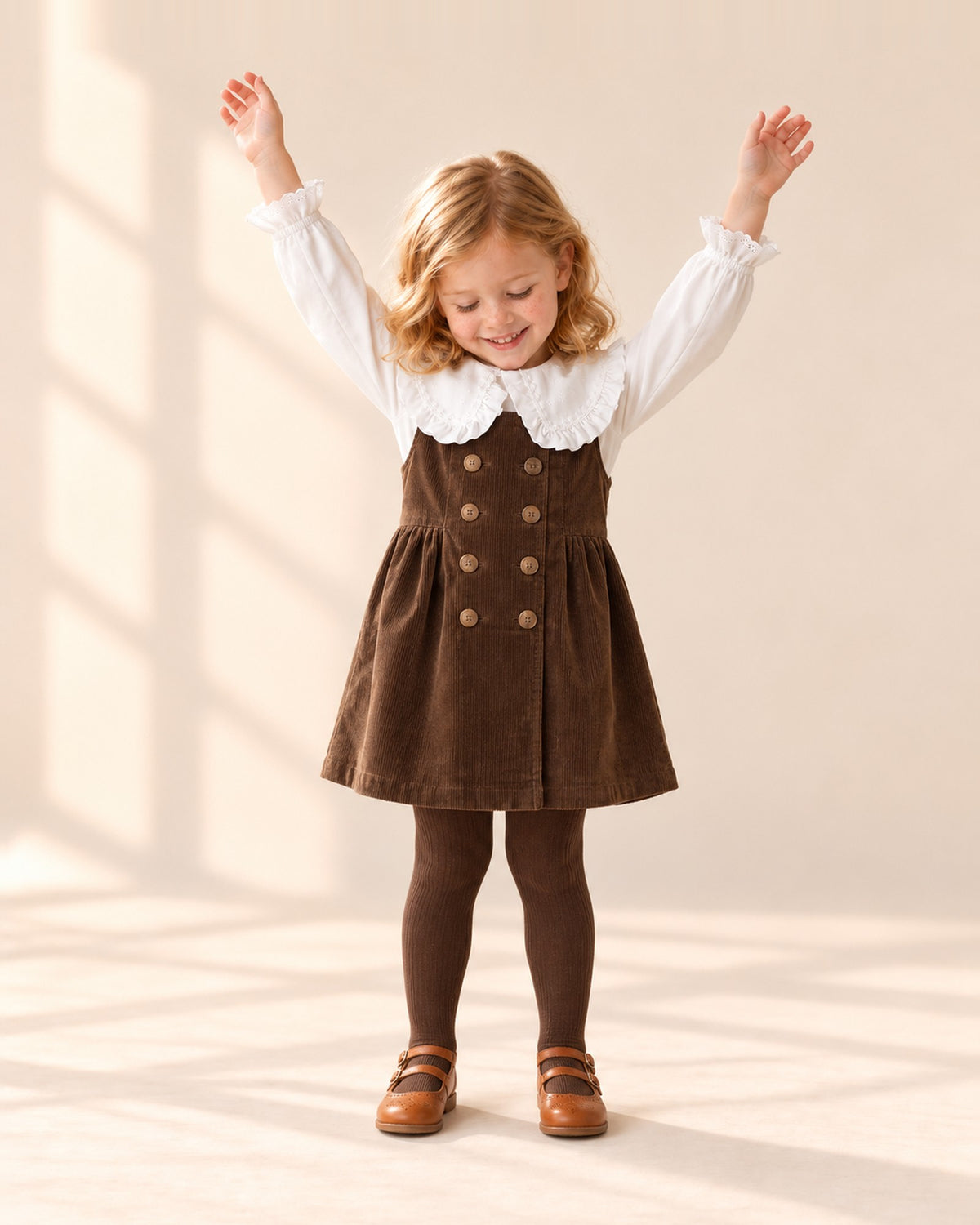 Girl sitting on a step in her corduroy pinafore outfit and cognac Mary Janes – Cognac