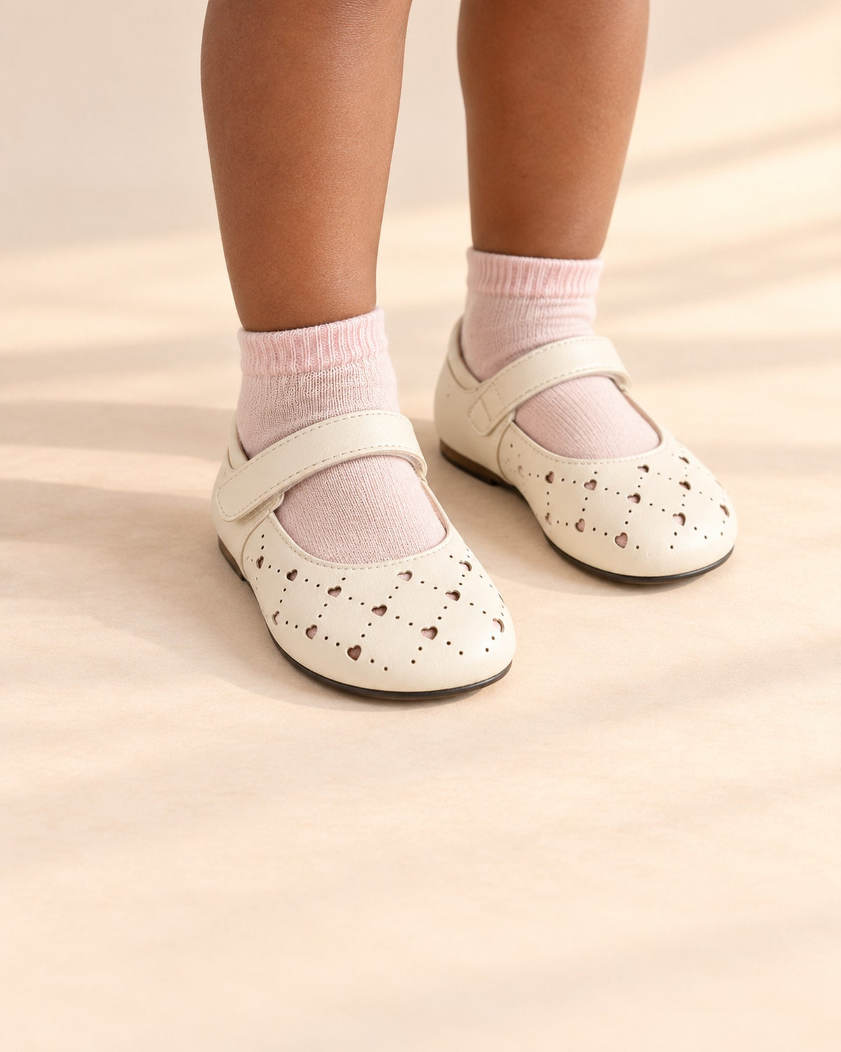 Close-up of a girl's feet in cream perforated Mary Janes with soft pink ankle socks – Cream