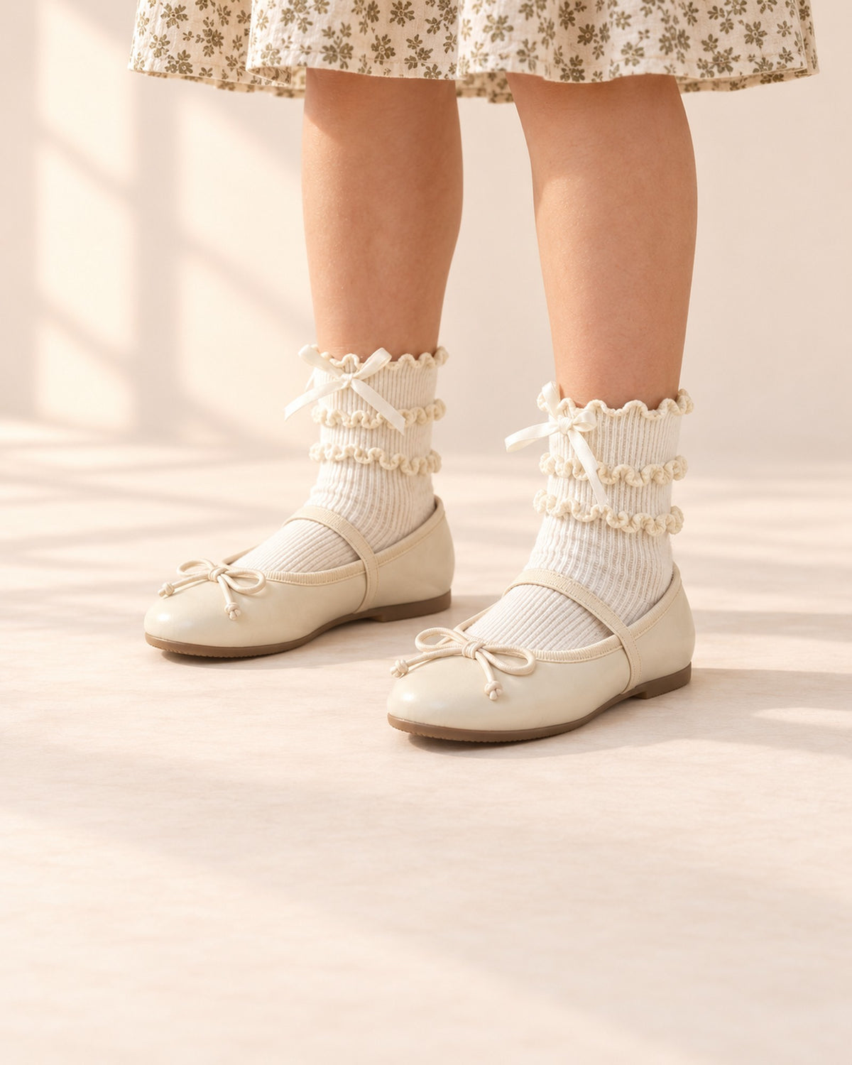 Close-up of a girl's legs from knee to floor in cream lace ruffle socks and cream bow flats – Cream