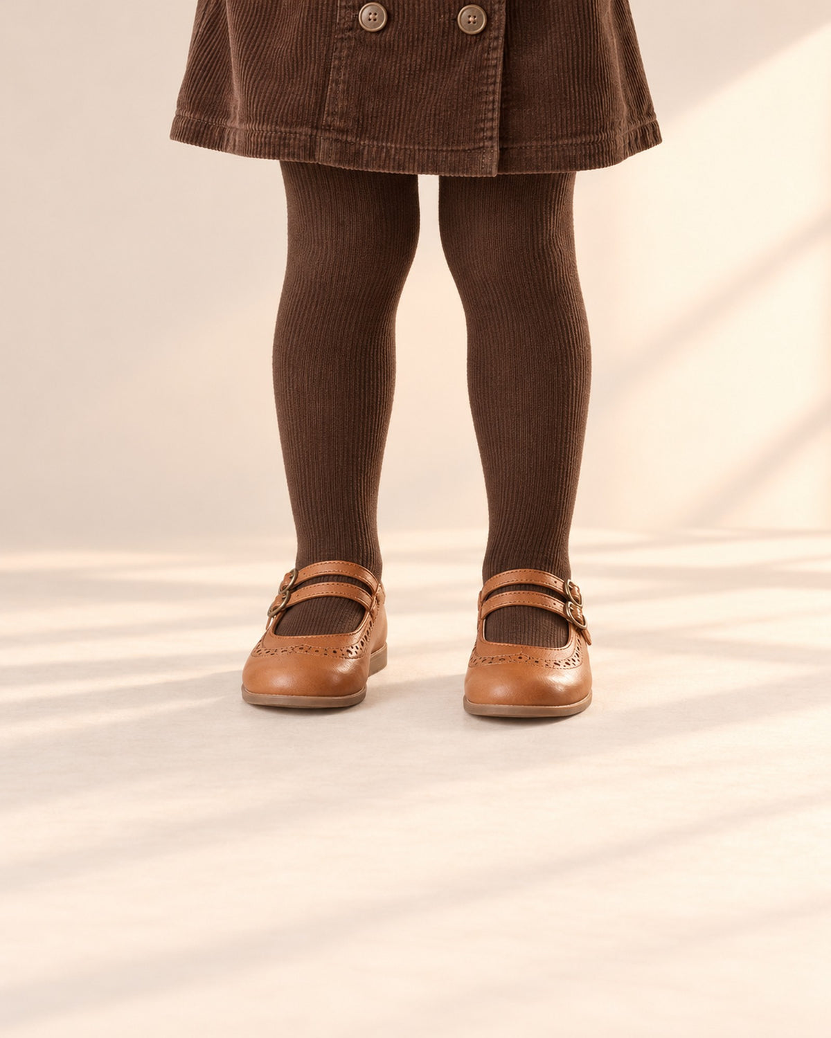 Close-up of a girl's legs from knee to floor in chocolate fine rib tights and cognac Mary Janes – Chocolate