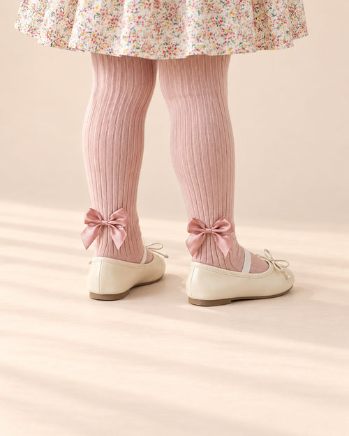 Close-up of a girl's legs from knee to floor in blush pink tights with satin ankle bows and cream flats – Blush Pink