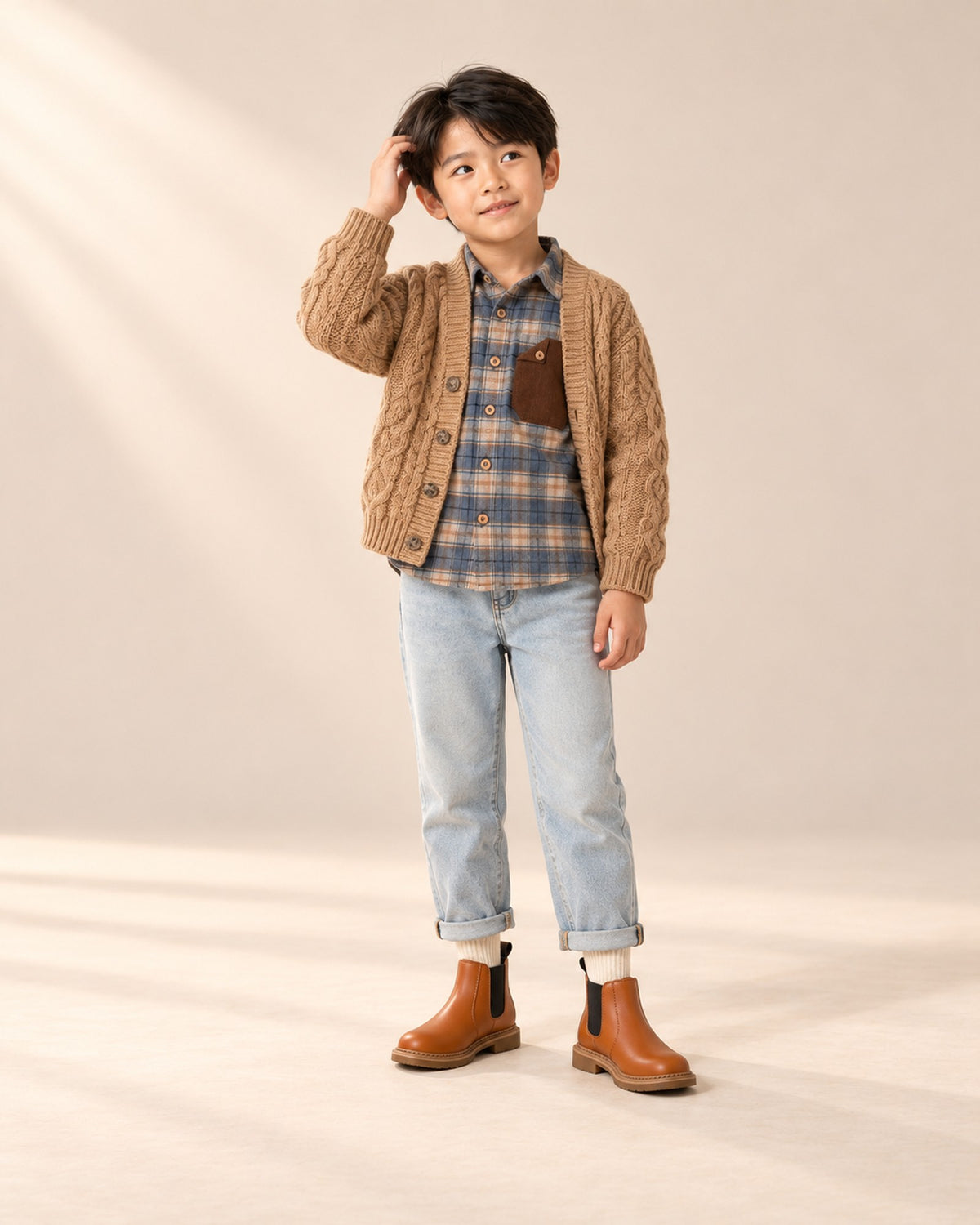 Front view of a boy in a blue plaid flannel shirt, camel cardigan, light-wash jeans and cognac boots, full length – Cream