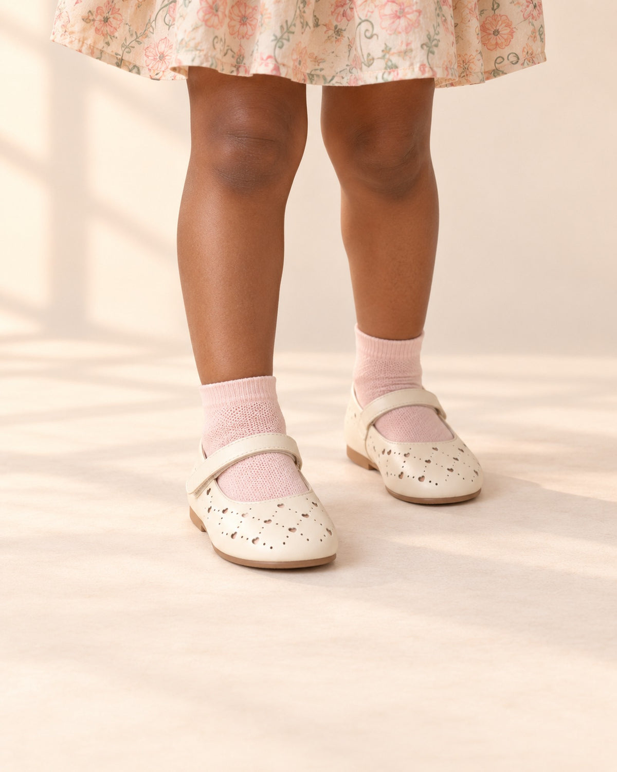 Close-up of a girl's legs from knee to floor in soft pink ankle socks and cream perforated Mary Janes – Soft Pink