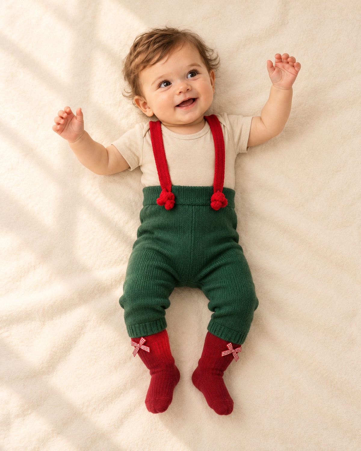 Front view of a baby in the green suspender pants, oatmeal bodysuit and red bow socks, full length – Green