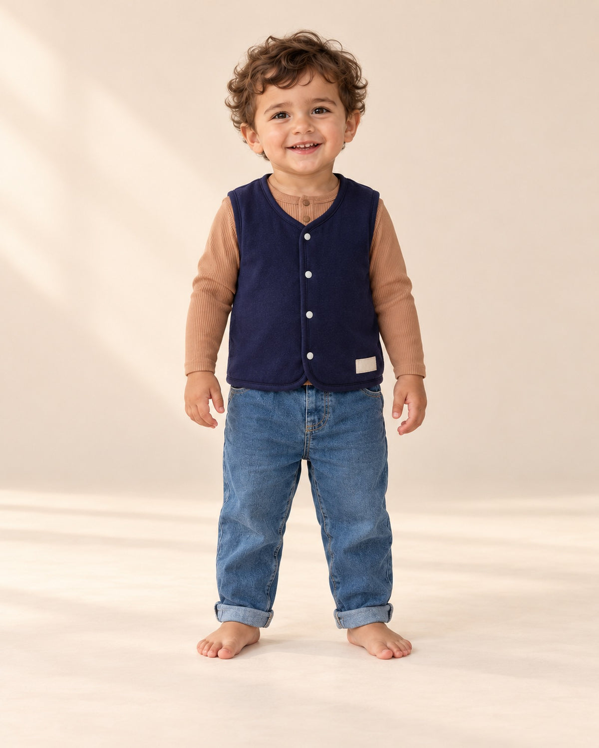 Front view of a little boy in the navy vest, caramel henley bodysuit and pull-on baby jeans, full length – Navy